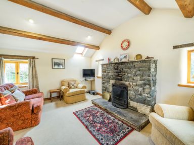 A living room with a stone fireplace wooden beams armchairs a sofa and a rug at Moresdale Bank Cottage Lambrigg near Sedbergh and Kendal