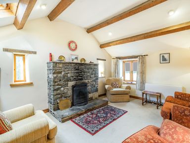 A living room with stone fireplace wooden beams armchairs and a rug at Moresdale Bank Cottage in Lambrigg near Sedbergh and Kendal