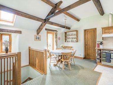 A dining area with a round table and wooden chairs near a wooden staircase and kitchen at Moresdale Bank Cottage Lambrigg near Sedbergh and Kendal