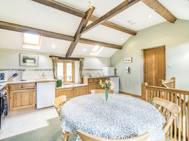 A kitchen with wooden cabinets a dining table with chairs and flowers on it at Moresdale Bank Cottage in Lambrigg near Sedbergh and Kendal