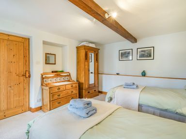 A bedroom with two single beds each with folded towels on top next to a wooden wardrobe and chest of drawers at Moresdale Bank Cottage in Lambrigg near Sedbergh and Kendal