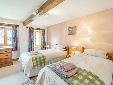 A bedroom with two single beds with folded towels and checkered blankets a wooden chest of drawers and two windows with colorful curtains at Moresdale Bank Cottage Lambrigg near Sedbergh and Kendal