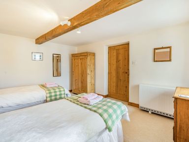 A bedroom with two single beds with green checkered blankets and towels a wooden wardrobe a wooden door a wall-mounted radiator and mirrors at Moresdale Bank Cottage Lambrigg near Sedbergh and Kendal