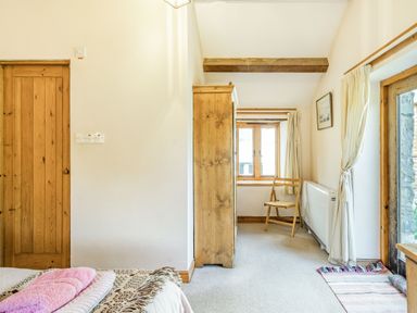 A bedroom with wooden furniture a wooden chair near window and glass door with curtains at Moresdale Bank Cottage in Lambrigg near Sedbergh and Kendal
