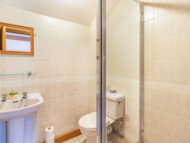 A bathroom with a pedestal sink, toilet, mirror, glass shelf, and shower enclosure at Moresdale Bank Cottage in Lambrigg near Sedbergh and Kendal