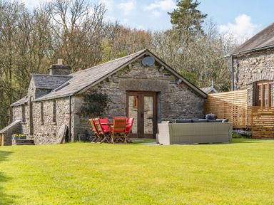 A stone cottage with a wooden table and red chairs and a sofa set on a grassy lawn at Moresdale Bank Cottage Lambrigg near Sedbergh and Kendal