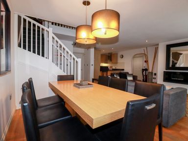 A dining area with a wooden table and black chairs near a staircase and a living room with a sofa at Lodge 22 Cherry Wadebridge