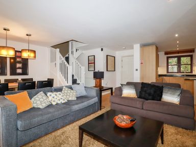 A living room with two sofas a coffee table and a dining area with chairs and lights at Lodge 22 Cherry in Wadebridge