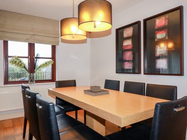 A dining room with a wooden table and black chairs under two hanging lamps and two framed artworks on the wall at Lodge 22 Cherry in Wadebridge