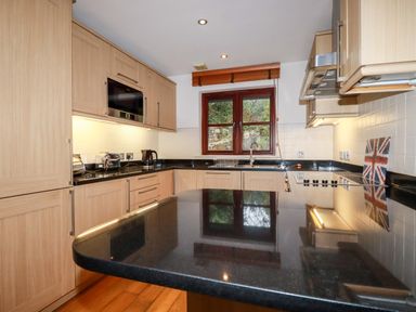 A kitchen with wooden cabinets black countertops and a window with a view at Lodge 22 Cherry in Wadebridge