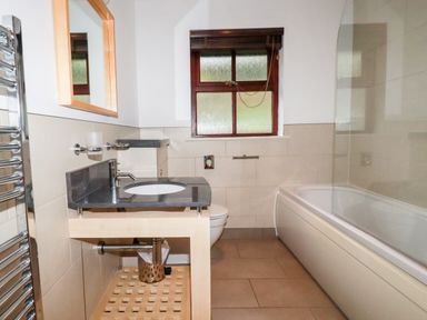 A bathroom with a sink on a wooden stand a toilet a bathtub with a glass screen and a window at Lodge 22 Cherry in Wadebridge