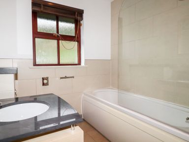 A bathroom with a bathtub shower and a sink under a window at Lodge 22 Cherry in Wadebridge