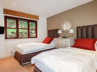 A bedroom with two single beds a nightstand with two lamps and a circular mirror at Lodge 22 Cherry in Wadebridge