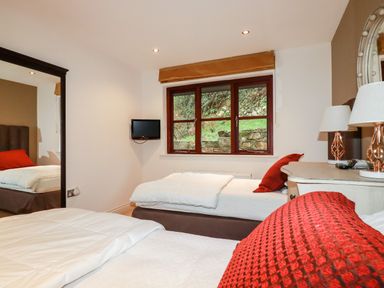 A bedroom with two single beds a window a wall-mounted television and a dresser with lamps at Lodge 22 Cherry in Wadebridge