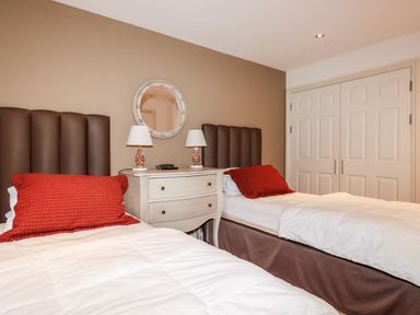 A bedroom with two beds white bedding red pillows a central white dresser and a round wall mirror at Lodge 22 Cherry in Wadebridge