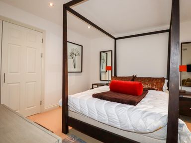 A bedroom with a four-poster bed a red pillow brown cushions bedside tables with lamps and framed floral artwork on the wall at Lodge 22 Cherry in Wadebridge