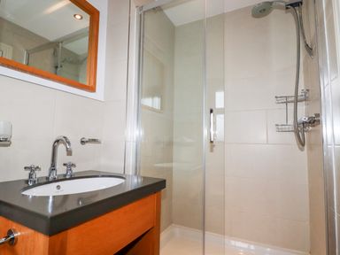A bathroom with a sink and mirror next to a glass shower enclosure at Lodge 22 Cherry in Wadebridge