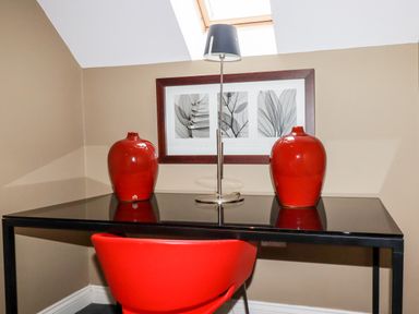 A black desk with two red vases a lamp and a framed picture above it with a red chair in a corner of a room at Lodge 22 Cherry Wadebridge
