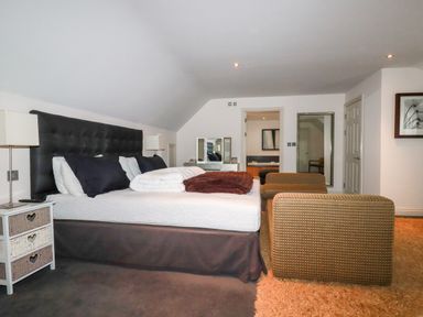 A bedroom with a large bed two bedside tables lamps two chairs a full length mirror and a dresser at Lodge 22 Cherry in Wadebridge