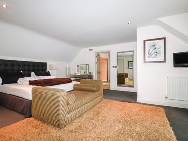 A bedroom with a double bed a vanity table a large mirror a wall-mounted TV and a patterned sofa at Lodge 22 Cherry in Wadebridge