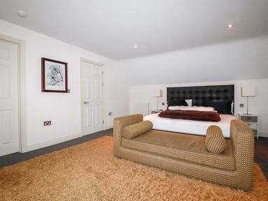 A bedroom with a large bed a padded bench a shaggy rug and artwork on the wall at Lodge 22 Cherry in Wadebridge