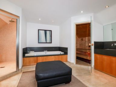 A bathroom with a bathtub, a glass door shower, a black ottoman, and a wooden sauna at Lodge 22 Cherry in Wadebridge