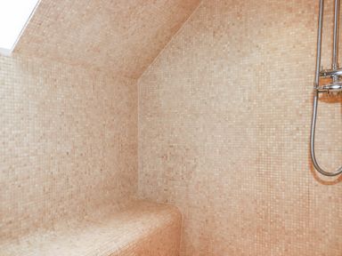 A shower area with small square beige tiles covering a built-in bench and walls and a shower fixture on the right at Lodge 22 Cherry in Wadebridge