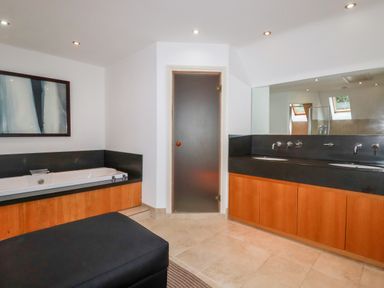 A bathroom with a bathtub wooden cabinets a double sink with a large mirror and a frosted glass door at Lodge 22 Cherry in Wadebridge