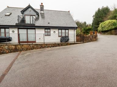 An exterior view of a house with a stone foundation railing and a driveway with trees and bushes at Lodge 22 Cherry in Wadebridge