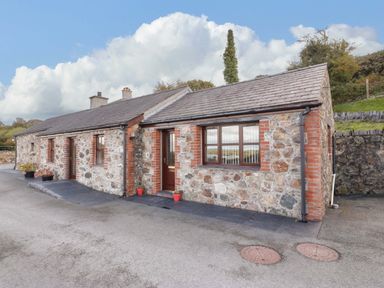 Stone cottage with multiple windows and a door on a paved driveway at Penrallt Cottage in Y Felinheli near Caernarfon