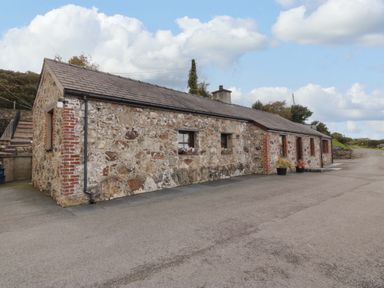 A stone cottage with small windows and flower pots outside on a paved area at Penrallt Cottage in Y Felinheli near Caernarfon