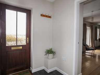 An entryway with a wooden door a potted plant on a small pedestal and a wooden coat rack at Penrallt Cottage in Y Felinheli near Caernarfon