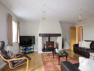 A living room with a fireplace television armchairs and a sofa at Penrallt Cottage in Y Felinheli near Caernarfon