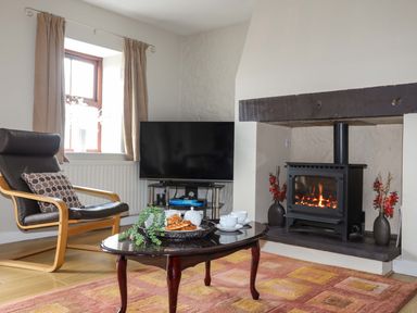 A living room with a fireplace a television a chair and a coffee table with cups and pastries at Penrallt Cottage in Y Felinheli near Caernarfon
