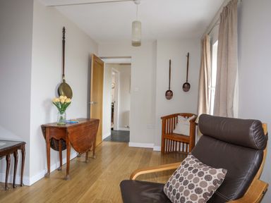 A sitting area with a brown leather chair wooden tables and wall hangings at Penrallt Cottage Y Felinheli near Caernarfon