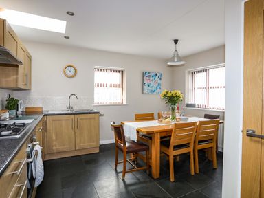 A kitchen with wooden cabinets a dining table with chairs and flowers at Penrallt Cottage in Y Felinheli near Caernarfon