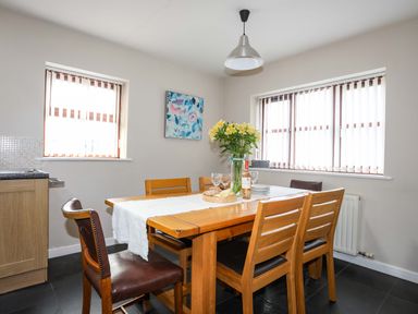 A dining room with a wooden table and chairs flowers and wine glasses on the table at Penrallt Cottage in Y Felinheli near Caernarfon