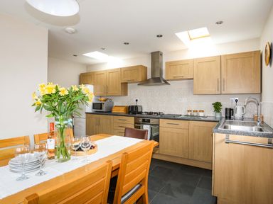 A kitchen with wooden cabinets and a dining table with flowers and wine at Penrallt Cottage in Y Felinheli near Caernarfon