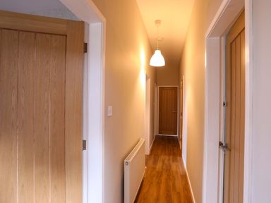 A hallway with wooden doors on both sides a radiator on the left wall and a ceiling light at Penrallt Cottage in Y Felinheli near Caernarfon