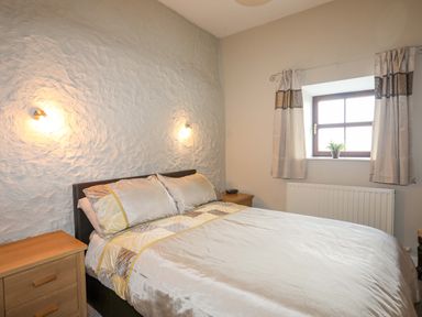 A bedroom with a double bed bedside tables a window with curtains and a plant at Penrallt Cottage in Y Felinheli near Caernarfon