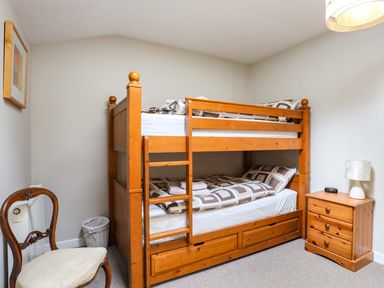 A bedroom with a wooden bunk bed a wooden chair a wooden nightstand with a lamp and a framed picture on the wall at Penrallt Cottage in Y Felinheli near Caernarfon