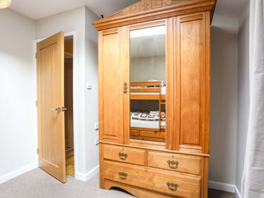 A wooden wardrobe with a mirror reflecting a bunk bed in a room with an open wooden door at Penrallt Cottage in Y Felinheli near Caernarfon