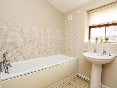 A bathroom with a bathtub and a pedestal sink under a window with small plants on the sill at Penrallt Cottage in Y Felinheli near Caernarfon