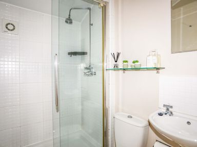 A bathroom with a glass shower enclosure a white sink toilet and a glass shelf with decor at Penrallt Cottage in Y Felinheli near Caernarfon