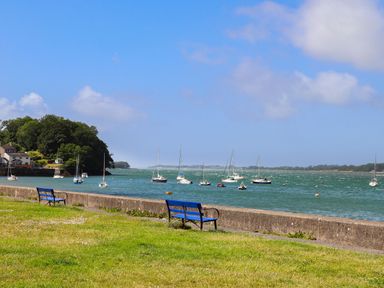 A waterfront with blue benches facing water and sailboats at Penrallt Cottage in Y Felinheli near Caernarfon