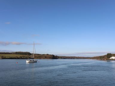 A body of water with a sailboat and houses in the distance at Penrallt Cottage in Y Felinheli near Caernarfon