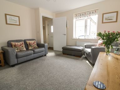A living room with two gray sofas a gray ottoman a wooden table with flowers and two framed pictures on the wall at Sandlings Hollesley near Woodbridge