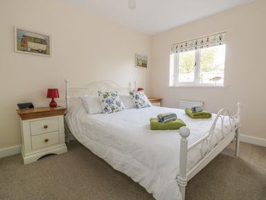 A bedroom with a white metal bed with floral pillows and green towels on the bed at Sandlings in Hollesley near Woodbridge