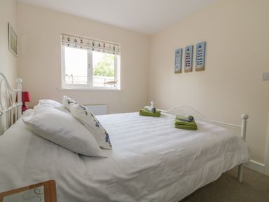 A bedroom with a white metal bed frame a window with patterned blind and three paintings on the wall at Sandlings Hollesley near Woodbridge