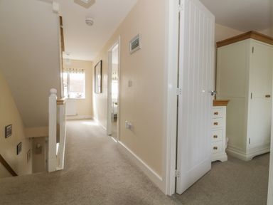 A carpeted hallway with a staircase and open doors leading to rooms at Sandlings Hollesley near Woodbridge